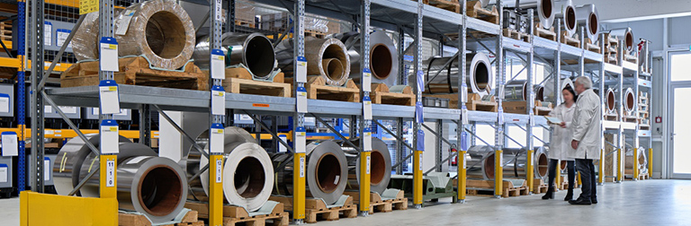 Mitarbeiter im Rohmateriallager vor Coils aus Edelstahl und anderen Metallen für den endlosen chemischen Reel-to-Reel Ätzprozess